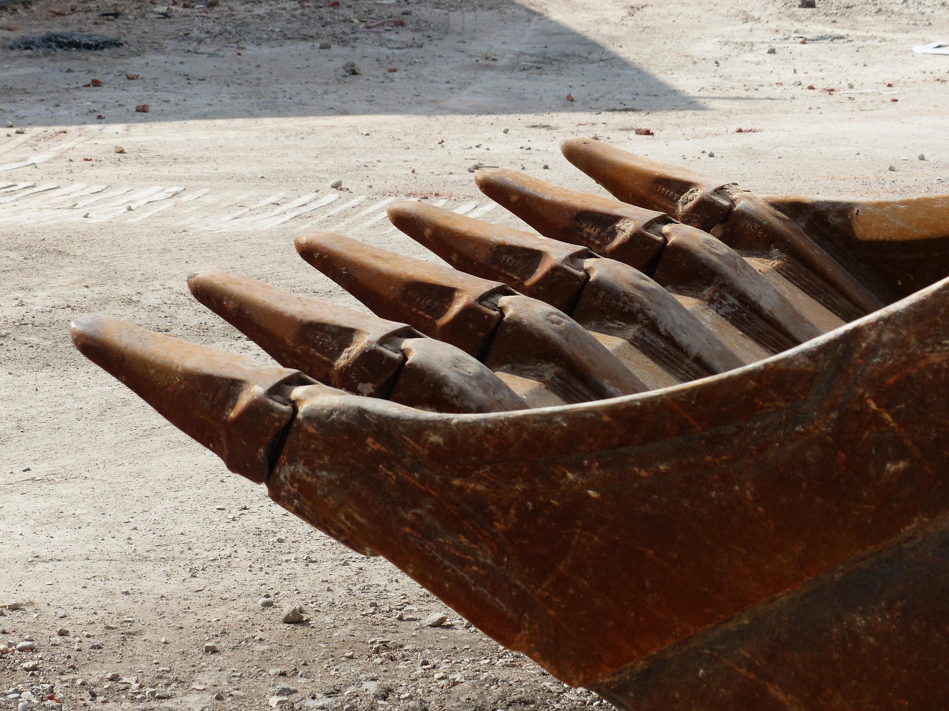 Cazoleta de excavadora con dientes de acero sobre terreno de obra